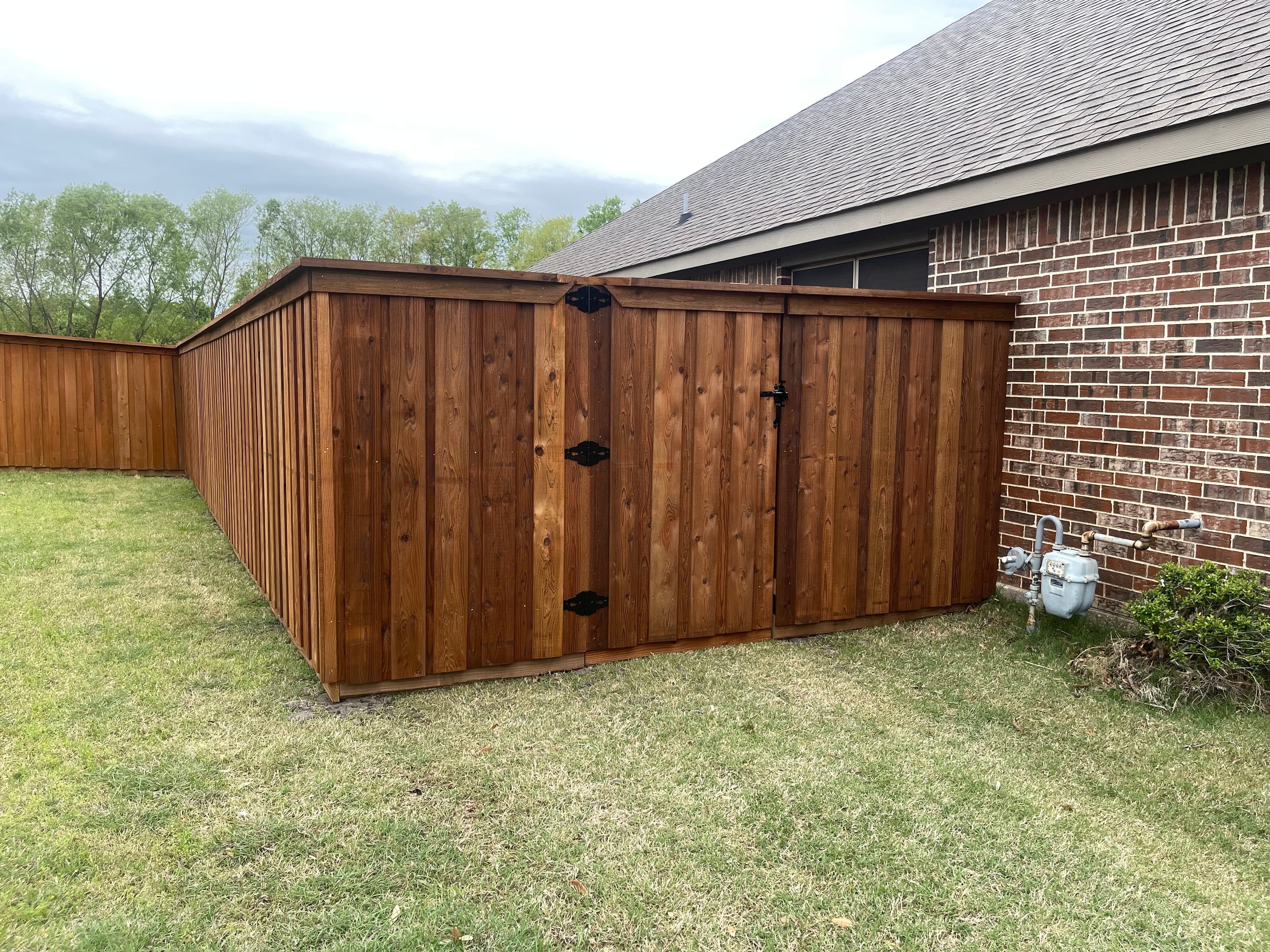 Wooden fence gate with black hardware next to brick home